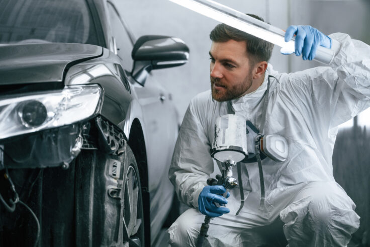 Man painting car with spray gun under lighting equipment