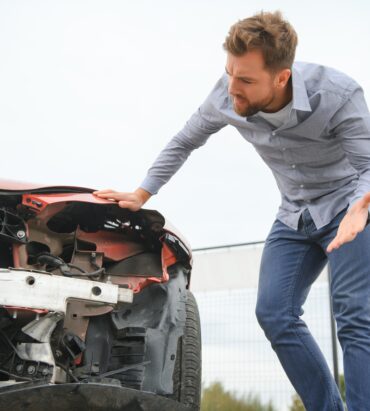 Damaged Car with Driver Looking On in Despair