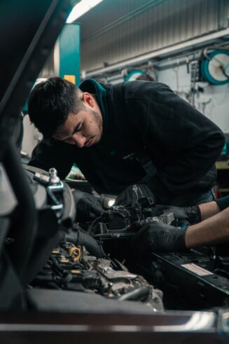 Two mechanics in black clothing working on engine